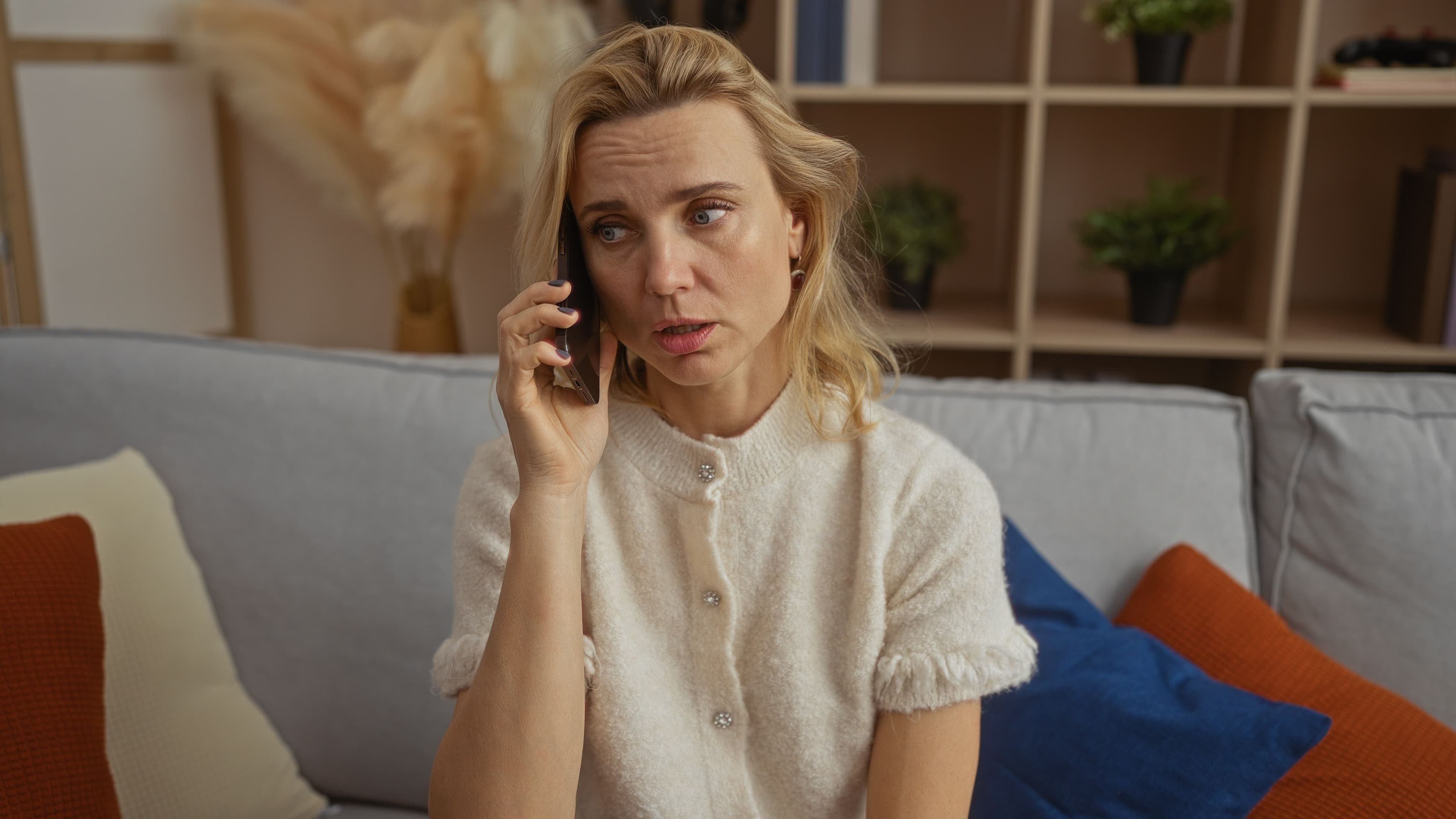 Woman looking worried while talking on phone in cozy living room setting with modern decor.