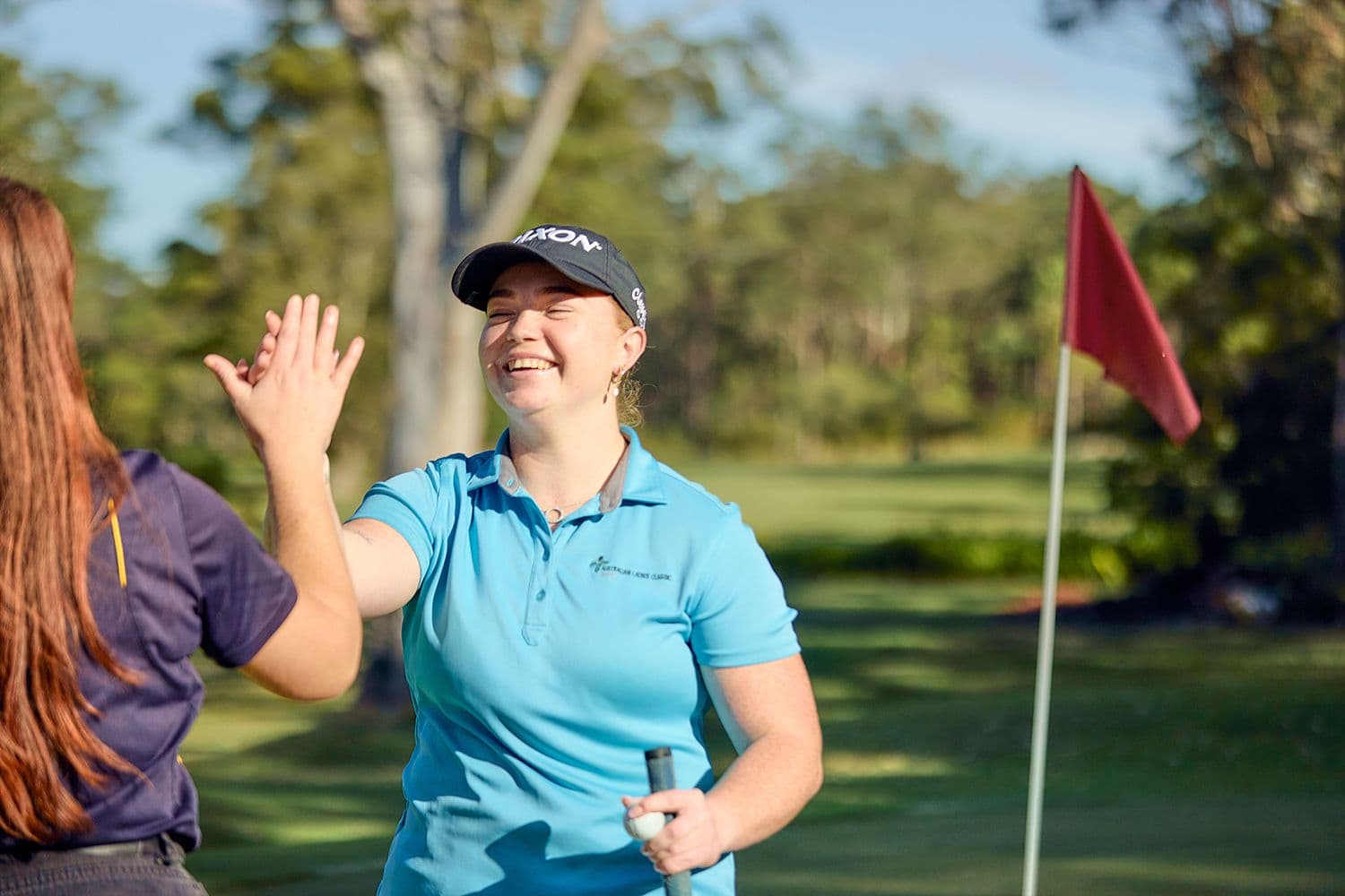 Two women high fiving at a golf course.